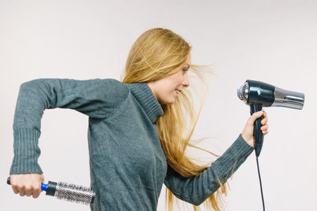 Female accessories holds hairdryer and round brush. Blonde woman styling her very long hair. side viewの写真素材