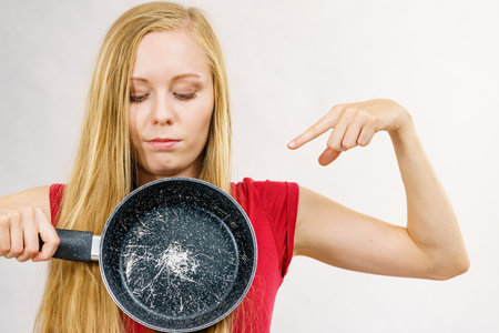 Woman holding scratched frying pan, cause of cancer. Torn coating, kitchen utensils is unusableの写真素材