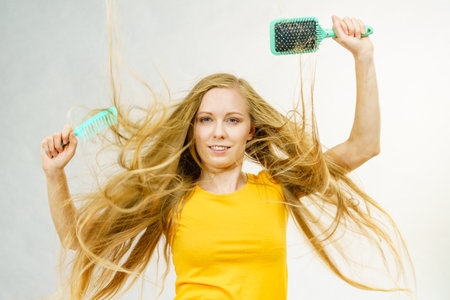 Girl with blowing long blonde hair holding brush and comb. Haircut, haircare concept.の写真素材
