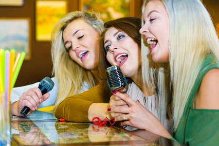 Women singing songs in karaoke club. Female friends with microphone having fun. Party, celebration, nightlife and people concept.の写真素材