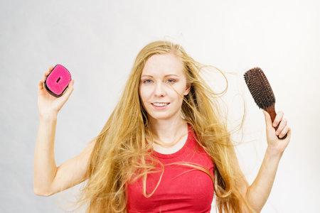 Blonde girl long blowing hair holds two brushes, one with natural bristles. Haircare, treatment concept.の写真素材