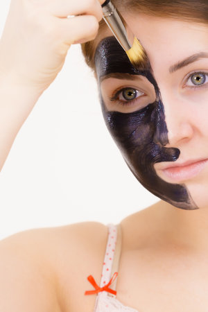 Skin care. Female applying black purifying mud mask, deep cleanser to her face, using brush. Beauty, spa and acne treatment.の写真素材