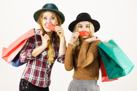 Female friends on shopping showing tag with sale percentage sign enjoying cheap clothing.の写真素材