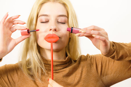 Young adult woman applying lipstick or lip gloss, getting her make up done holding fake lips on stickの写真素材