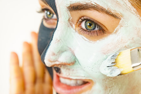 skincare. Female applying green purifying mud mask, cosmetic healing clay to face, using brush. Beauty and wellness. Spa and acne treatment.の写真素材