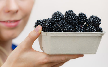 Girl holding fresh blackberry fruits in paper box. Healthy seasonal fruit, organic nutrition.の写真素材