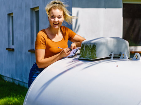 Woman checking level of propane gas in tank in yard of single family house. Home heating.の写真素材
