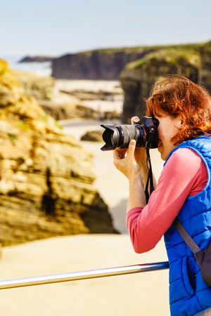 Tourist woman taking travel photo from sea coast landscape, cliff formations on Cathedral Beach in Galicia Spain. Playa de las Catedrales, As Catedrais in Ribadeo, province of Lugo.の写真素材