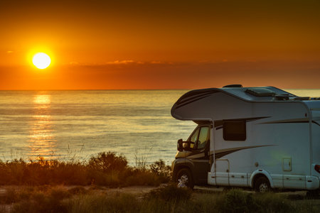 Sun rising over sea horizon, day break and caravan parking on beach sea shore. Travel with mobile home.の写真素材