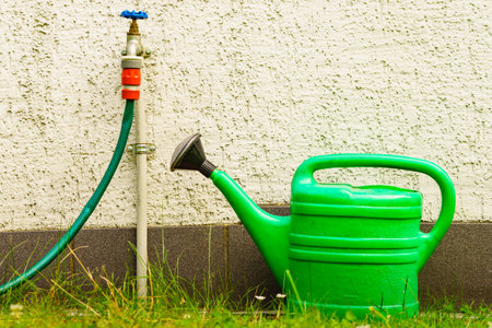 Gardening tools watering green can and tap with hose on garden plot.の写真素材