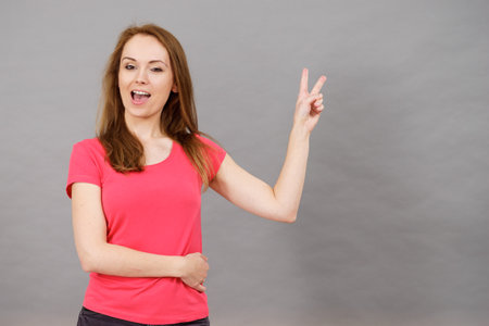 Young happy excited woman winking, doing victory gesture sign. Satisfaction success and celebrating.の写真素材
