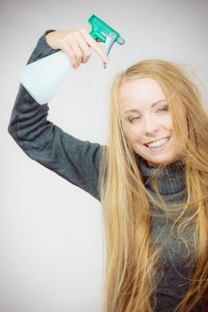 Young female messy long blonde hair holding bottle, applying hair spray.の写真素材