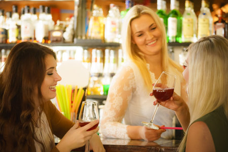 Happy young women with wine alcohol glasses in pub at counter with bar employee. Celebration, friends and relaxation time.の写真素材