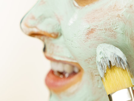 skincare. Female applying green purifying mud mask, cosmetic healing clay to face, using brush. Beauty and wellness. Spa and acne treatment.の写真素材