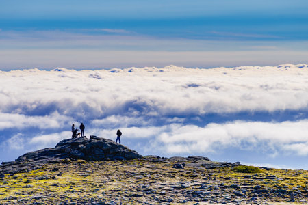 Hikers in silhouette stands on rock in mountains above clouds. Torre mountain peak, Serra da Estrela, the highest place in Continental Portugal.の写真素材