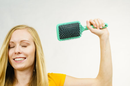 Blonde girl with brush combing her long hair. Girl taking care refreshing her hairstyle. Haircare concept.の写真素材