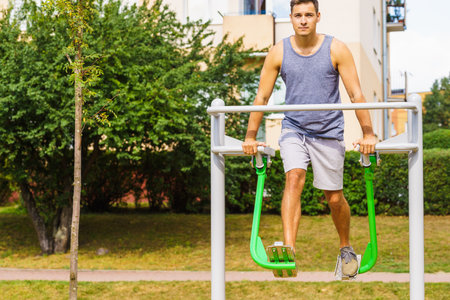 Young man working out in outdoor gym, doing legs exercises on public machine in park. Staying fit and healthy.の写真素材