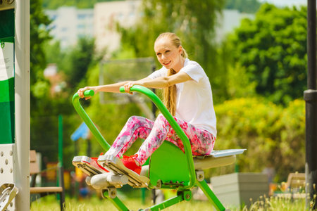 Young woman working out in the outdoor gym. Girl making exercises and training at public sport area in city park. Healthy lifestyle.の写真素材