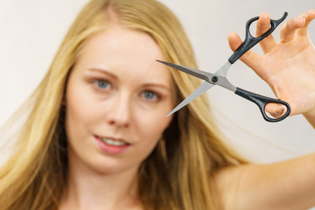 Young woman holding shears tool ready to hair trimming. Blonde female with scissors creating new hairdo coiffure. Hairstyle and haircut.の写真素材