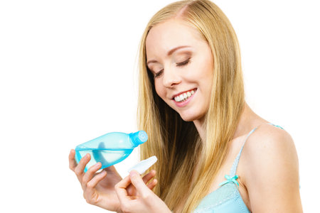 Skincare. Young woman holding bottle with tonic cosmetic, cleaning skin with cotton pad. Girl taking care of her body.の写真素材
