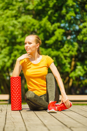 Young woman exercises in park, using gym accessory, foam roller for muscle massage. Staying fit and healthy.の写真素材
