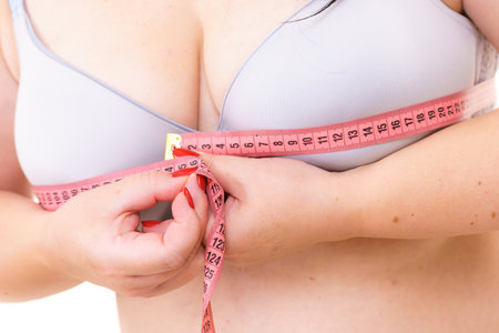 Closeup of female breasts. Plus size fat woman wearing bra using tape measure to check the measurements of her big chest. Bosom, brafitting and underwear concept.の写真素材
