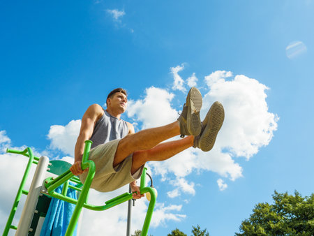 Young man working out in outdoor gym, doing leg lifting abs exercise. Staying fit and healthy.の写真素材