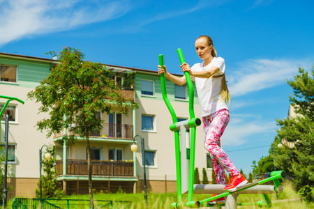 Young woman doing exercises on public equipment in city park. Girl working out training in outdoor gym. Healthy lifestyle.の写真素材