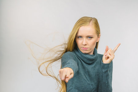 Young woman pointing at you and weighing her finger. Rejecting gesture, disagree sign. Serious face expression.の写真素材