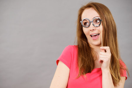 Happy woman holding fake eyeglasses on stick having fun. Photo and carnival funny accessories concept.の写真素材