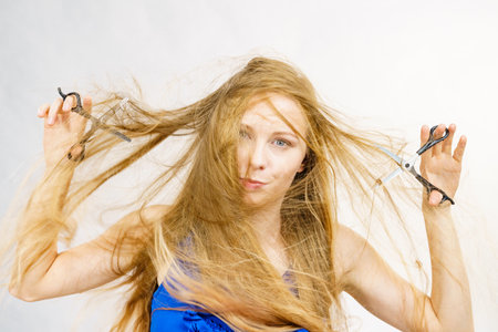 Haircut coiffure haircare concept. Girl with blowing long blond hair holding scissors, showing work tools, normal and thinning shears.の写真素材