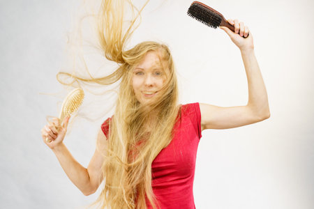 Blonde girl long blowing hair holds two brushes, one with natural bristles. Haircare, treatment concept.の写真素材