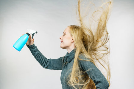 Young female messy long blonde hair holding bottle, applying thermal protect hair spray. Side viewの写真素材