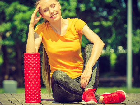 Young woman exercises in park, using gym accessory, foam roller for muscle massage. Staying fit and healthy.の写真素材