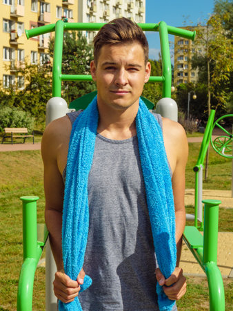 Handsome guy relaxing after outdoor workout. Fit man feeling healthy, enjoying sun. Exercising on public gym equipment in the open air.の写真素材