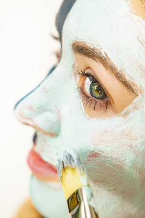 skincare. Female applying green purifying mud mask, cosmetic healing clay to face, using brush. Beauty and wellness. Spa and acne treatment.の写真素材