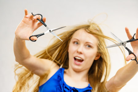 Haircut coiffure haircare concept. Girl with blowing long blond hair holding scissors, showing work tools, normal and thinning shears.の写真素材