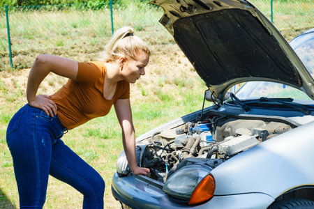 Woman having trouble with broken car, looking inside at failed engine. Breakdown car.の写真素材