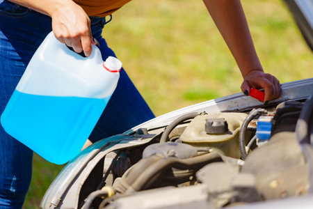 Woman pouring blue antifreeze liquid for car windshield screen washing with bootle watering canの写真素材
