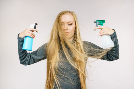 Young female messy long blonde hair holding bottle, applying hair spray.の写真素材