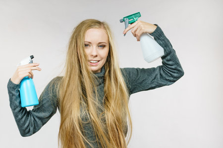 Young female messy long blonde hair holding bottle, applying hair spray.の写真素材