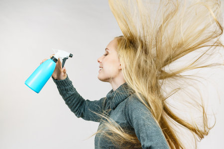 Young female messy long blonde hair holding bottle, applying thermal protect hair spray. Side viewの写真素材