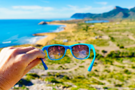 Hand holding sunglasses against spanish sea coast. Travel and holidays.の写真素材
