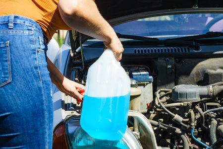 Woman pouring blue antifreeze liquid for auto windshield screen washing with bottle watering can.の写真素材