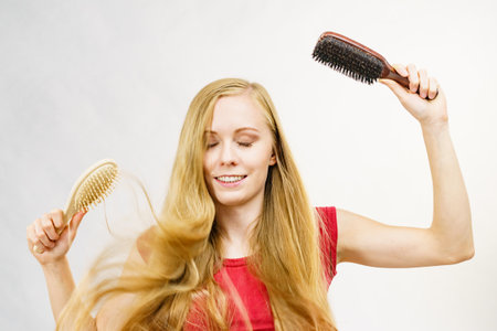 Blonde girl with brush combing her long hair. Girl taking care refreshing her hairstyle. Beauty, treatment and haircare.の写真素材