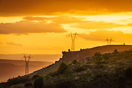 Electricity transmission pylons, power lines high voltage towers in mountains at sunset.の写真素材
