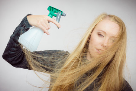 Young female messy long blonde hair holding bottle, applying hair spray.の写真素材
