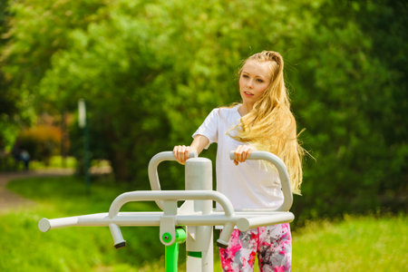 Young woman working out outside. Girl making exercises and training on public equipment in outdoor gym at park. Healthy lifestyle.の写真素材