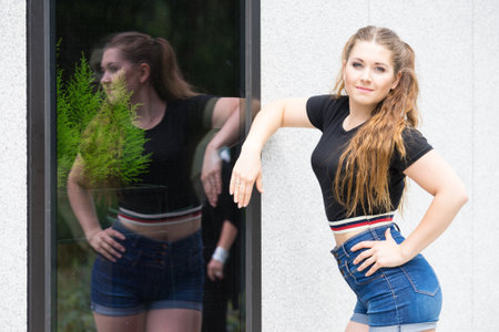 Young teenage woman wearing denim shorts and black crop top. Female presenting fashionable summer outfit.の写真素材