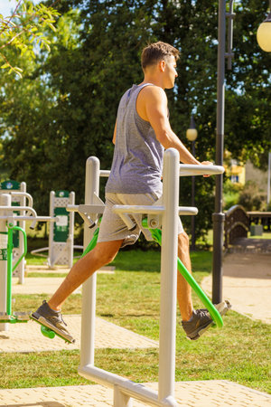 Young man working out in outdoor gym, doing legs exercises on public machine in park. Staying fit and healthy.の写真素材